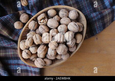 Vue d'en haut d'un panier de noix en coque, sur une table en bois avec un fond de tartan dans tons rustiques. La nature des aliments. Avec copyspace Banque D'Images