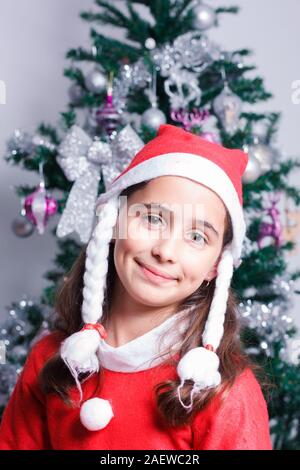 Portrait of happy girl dressed as Santa Claus à côté d'arbre de Noël. Banque D'Images