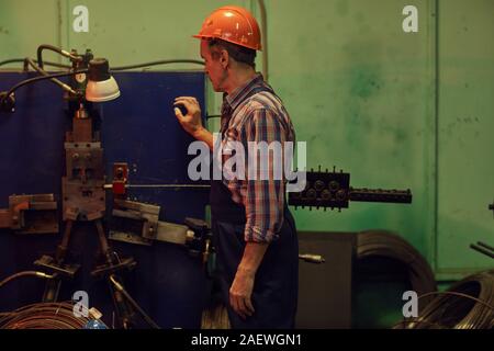 Ingénieur Travaux en maturité helmet, debout près de la machine et de contrôler le travail de celui-ci tout en travaillant dans l'usine Banque D'Images