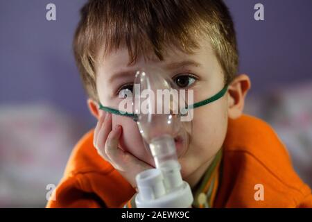 Petit garçon dans un masque, les traitements des voies respiratoires avec  un pulvérisateur à la maison. Siège bébé avec un nébulisateur dans sa  bouche, inhalateur, le traitement de la bronchite Photo Stock 