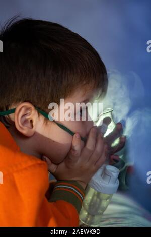 Petit garçon dans un masque, les traitements des voies respiratoires avec  un pulvérisateur à la maison. Siège bébé avec un nébulisateur dans sa  bouche, inhalateur, le traitement de la bronchite Photo Stock 