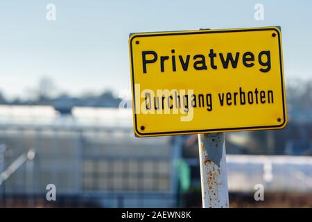 Panneau jaune avec texte allemand 'chemin privé entrée interdite' sur une journée ensoleillée. Out-of-focus comme arrière-plan de construction - gros plan, format paysage Banque D'Images