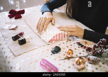 Femme attendent à manucure nail salon. Les mains des femmes sur la table de salon de beauté avec le vernis à ongles rouge et blanc, des échantillons, des boules de Noël et des lumières, w Banque D'Images