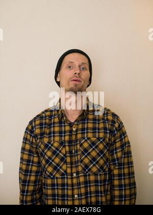 Jeune homme, modèle de la mode, portant une chemise à carreaux avec un aveugle beige derrière lui. Guy in black hat avec barbe dans un style décontracté. Banque D'Images