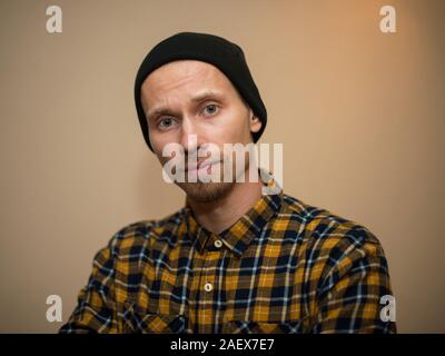 Jeune homme, modèle de la mode, portant une chemise à carreaux avec un aveugle beige derrière lui. Guy in black hat avec barbe dans un style décontracté. Banque D'Images