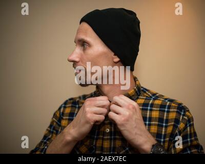 Jeune homme, modèle de la mode, portant une chemise à carreaux avec un aveugle beige derrière lui. Guy in black hat avec barbe dans un style décontracté. Banque D'Images