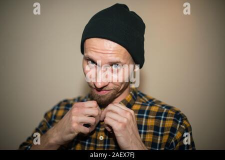 Jeune homme, modèle de la mode, portant une chemise à carreaux avec un aveugle beige derrière lui. Guy in black hat avec barbe dans un style décontracté. Banque D'Images