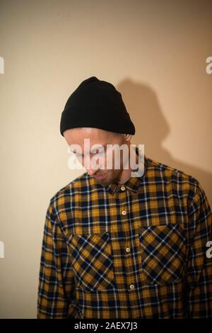 Jeune homme, modèle de la mode, portant une chemise à carreaux avec un aveugle beige derrière lui. Guy in black hat avec barbe dans un style décontracté. Banque D'Images