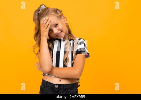 Fille blonde dans un noir et blanc à rayures T-shirt est titulaire d'une main près de sa tête sur un fond jaune Banque D'Images