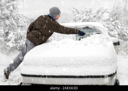 Jeune homme au brossage de la neige de sa voiture lors d'une froide journée d'hiver de neige Banque D'Images