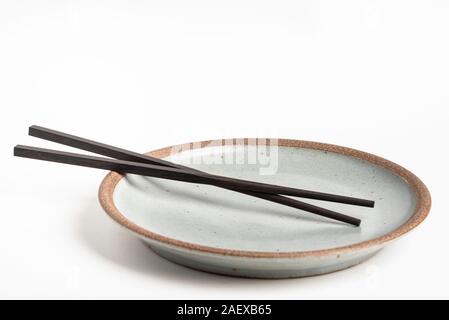 Une paire de baguettes en bois noir oriental repose sur une plaque de grès texturé et mis sur un fond blanc. Banque D'Images