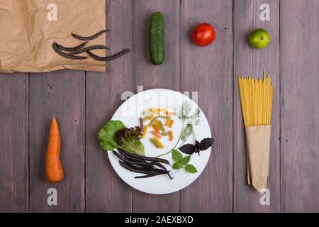 Pâtes fraîches ingrédients dans des sacs en papier écologique - pâtes spaghetti, carotte, basilic, tomates et autres légumes sur plaque sur table en bois Banque D'Images