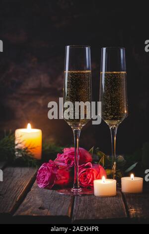 Deux verres de champagne avec des roses et des bougies allumées sur une table en bois rustique et d'arrière-plan Banque D'Images