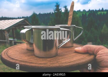 Le café du matin dans les tasses sur un plateau en bois dans une main d'homme dans le contexte de la forêt dans les montagnes Banque D'Images