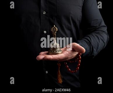 Homme adulte dans une chemise noire détient un rituel tibétain en cuivre bell, bell. low key représente le principe féminin d'excellence dans la sagesse. Banque D'Images