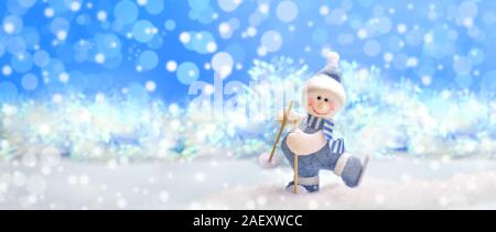 Bannière de fête de Noël. Décorations de Noël. Toy snowman feutrée en skis sur la neige sur fond de Noël bleu avec effet bokeh. Banque D'Images