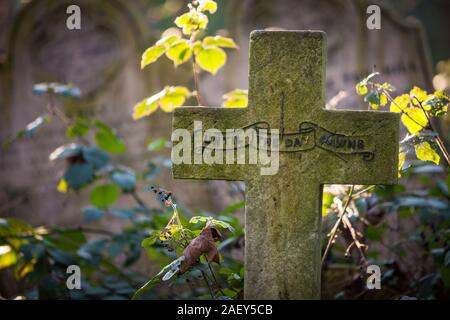 Cimetière anglais. Un crucifix en pierre solitaire pierre tombale dans un vieux cimetière envahi inscrit avec la phrase 'jusqu'à ce que le jour se lève' Banque D'Images