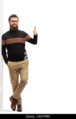 Portrait d'un homme barbu dans un Pull col roulé appuyée sur un mur et showing thumb up sign isolé sur fond blanc Banque D'Images