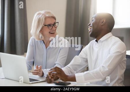 Smiling divers collègues rient coopérant au laptop in office Banque D'Images