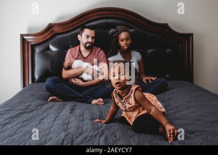 Assis sur le lit de la famille multiraciale avec jeune fille et l'enfant Banque D'Images