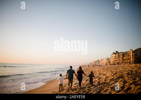 Famille de quatre marche loin sur la plage, main dans la main au coucher du soleil Banque D'Images