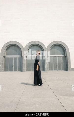 Jeune femme en longue robe noire devant les portes de l'immeuble Banque D'Images