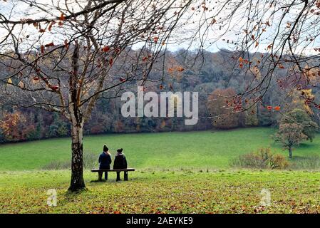 Deux femmes d'âge moyen s'asseoir sur le siège à l'échelle d'un paysage d'hiver dans les collines du Surrey à Ranmore Common près de Dorking England UK Banque D'Images