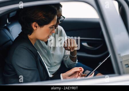 Deux collègues femmes looking at digital tablet et parler tout en séance d'une banquette arrière d'un taxi Banque D'Images