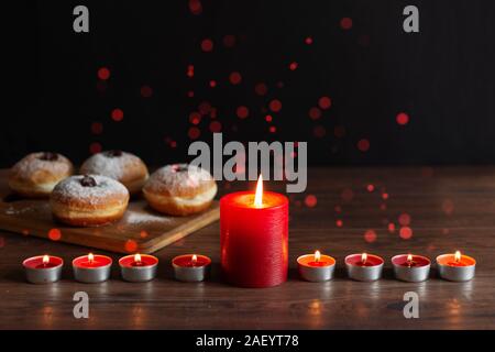 La menorah (chandelier traditionnel avec des bougies) et des beignets traditionnels sufganiyot sur table en bois pour la célébration de Hanoukka. Banque D'Images