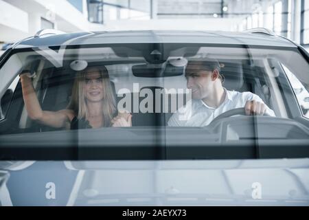 Guy ressemble à fille. Gestionnaire positif montrant les caractéristiques de la nouvelle voiture pour la clientèle féminine Banque D'Images