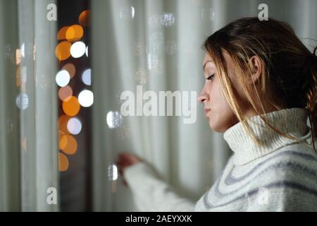 Triste femme seule se plaindre standing looking at les lumières de la ville, à travers une fenêtre dans la nuit à la maison Banque D'Images