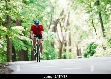 Homme barbu. Cycliste sur un vélo est sur la route asphaltée dans la forêt la journée ensoleillée Banque D'Images