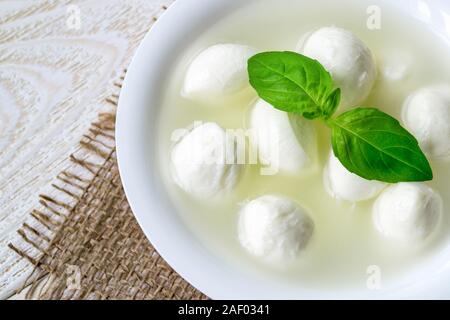 Close-up of bowl avec mini boules de fromage mozzarella dans la saumure et basilic blanc sur une table en bois rustique. Une cuisine méditerranéenne d'appui. Banque D'Images