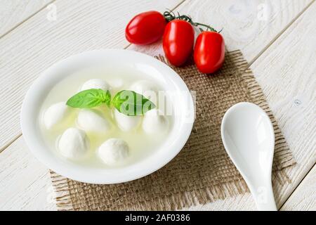 Boules de fromage mozzarella Mini avec de la saumure, trois tomates cerises rouges et cuillère en porcelaine blanche sur une table en bois rustique. Une cuisine méditerranéenne d'appui. Banque D'Images