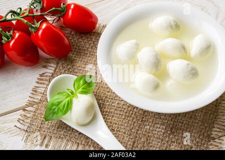 La saumure avec mini boules de fromage mozzarella dans un bol, une boule de mozzarella et basilic dans une cuillère et de la direction générale de tomates cerises rouges. Une cuisine méditerranéenne. Banque D'Images