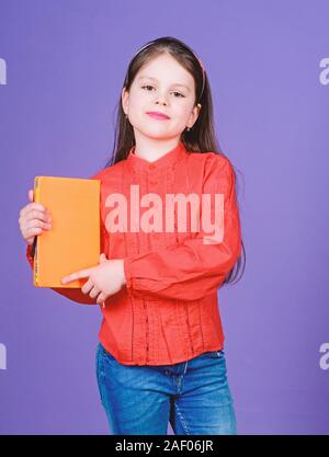 Confiant dans sa connaissance. Adorable petite fille tenant livre avec couvercle orange. Enfant mignon petit livre avec la connaissance dans les mains. Connaissances et compétences. Jour des connaissances ou le 1 septembre, l'espace de copie. Banque D'Images