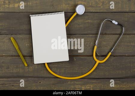 Concept de soins médicaux et de santé - jaune stéthoscope et bloc-notes à spirale blanche sur fond de bois. Voir mise à plat Banque D'Images