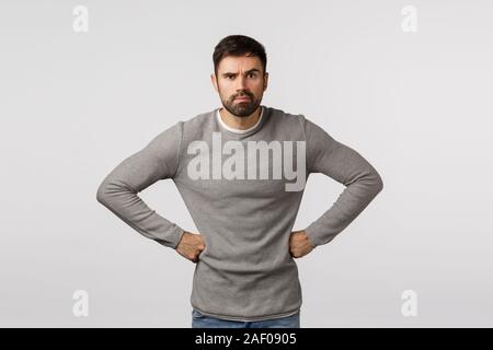 En colère et grincheuse, mécontent ou strict avec des hommes sérieux, porter la barbe chandail gris, tenant les mains sur la taille en exigeant, déçu posent, fronçant Banque D'Images