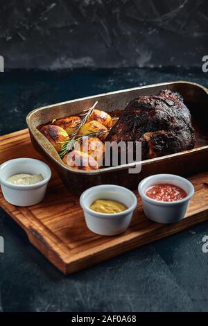 Un grand morceau de viande cuit au four avec des pommes de terre sur un plateau avec des sauces Banque D'Images