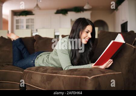 Femme lisant un livre sur son canapé à la maison Banque D'Images