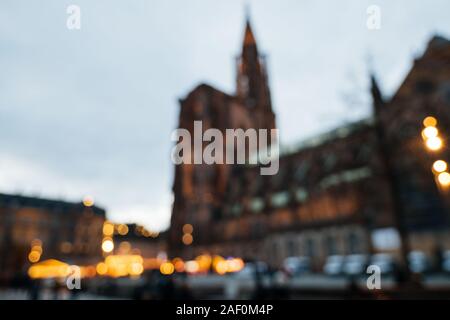 Flou flou artistique silhouettes de personnes réunis à la place de la cathédrale en face de l'église Notre-Dame dans le centre de Strasbourg pendant le marché de Noël annuel de la surveillance de la police cars en arrière-plan. Banque D'Images