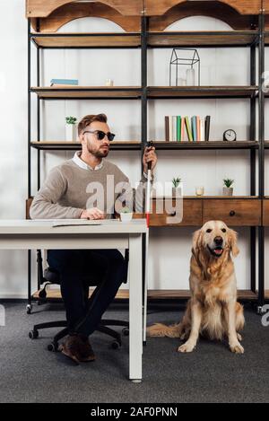 Aveugle avec bâton de marche assis à table à côté de golden retriever Banque D'Images