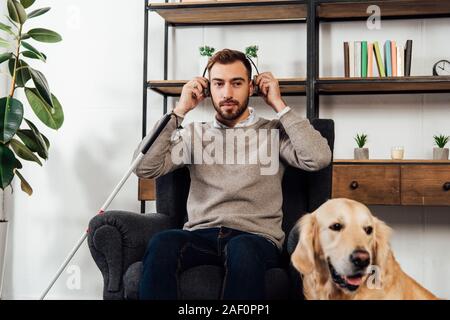 Les déficients visuels d'utiliser un casque homme à côté de golden retriever à la maison Banque D'Images