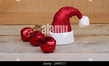 Santa hat rouge et blanc à côté de trois Jingle bells sur un fond de bois avec l'espace d'écriture Banque D'Images