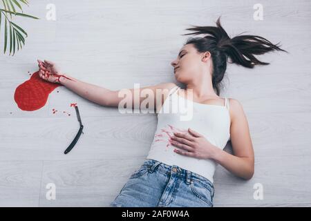 Vue aérienne de femme sans vie à couper les veines saignement lying on floor près de rasoir droit et flaque de sang Banque D'Images