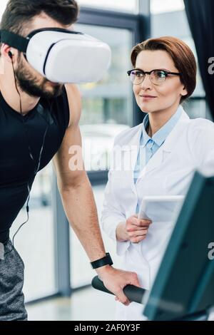 Sportsman s'exécutant sur un tapis roulant près de médecin avec tablette numérique pendant une épreuve d'endurance dans les sports center Banque D'Images