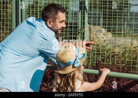 Bel homme pointant du doigt avec cage en se tenant debout avec sa fille au zoo Banque D'Images