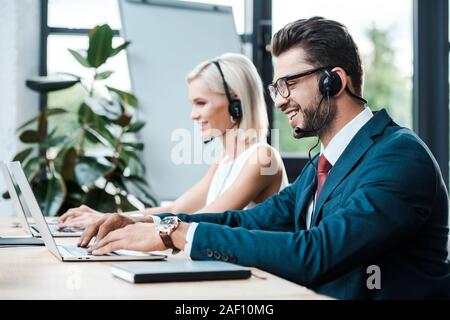 Focus sélectif des professionnels exploitant en typing on laptop casque près de blonde collègue dans le casque Banque D'Images