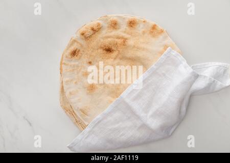 Vue de dessus du pain lavash plat recouvert d'une serviette blanche sur la surface en marbre Banque D'Images