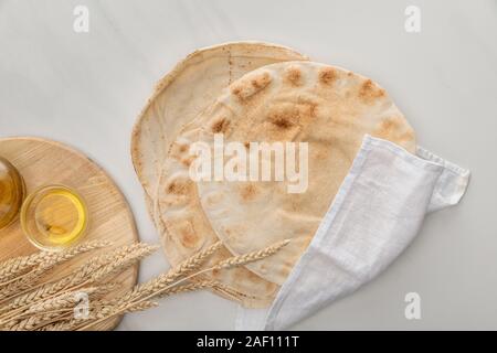 Vue de dessus du pain lavash plate recouverte de serviette blanche près de découper avec des clous et de l'huile sur la surface de marbre Banque D'Images